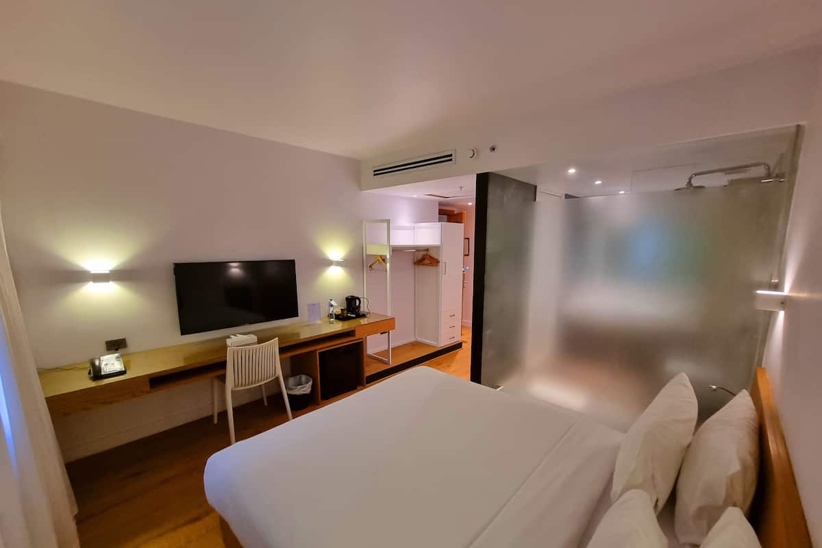 A hotel room with a bed, a desk with a TV, a chair, and a wardrobe.