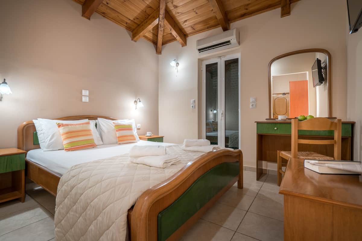 A bedroom with a wooden bed, a green headboard, a wooden desk, and a mirror.
