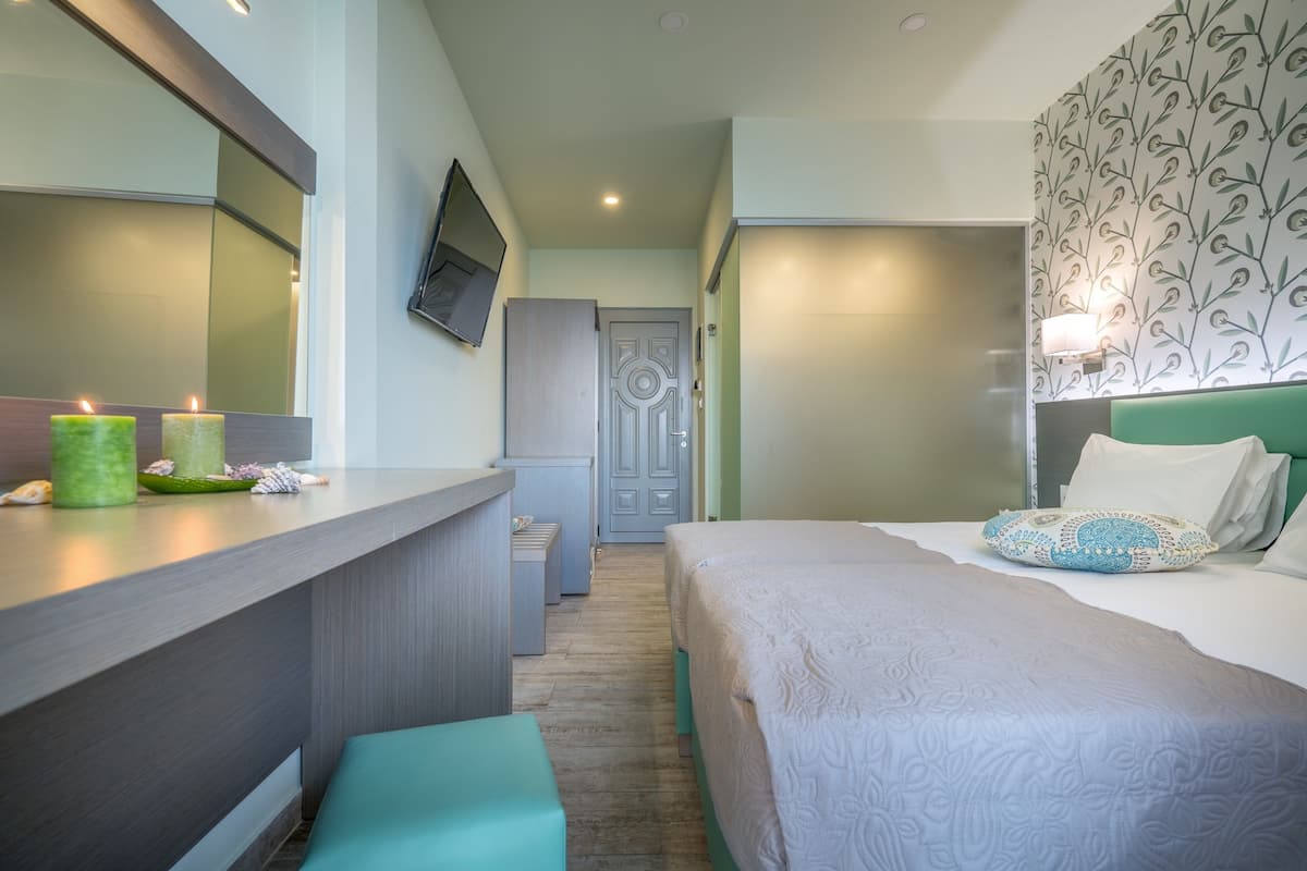 A hotel room with a bed, a desk with a mirror, a television, and a door.