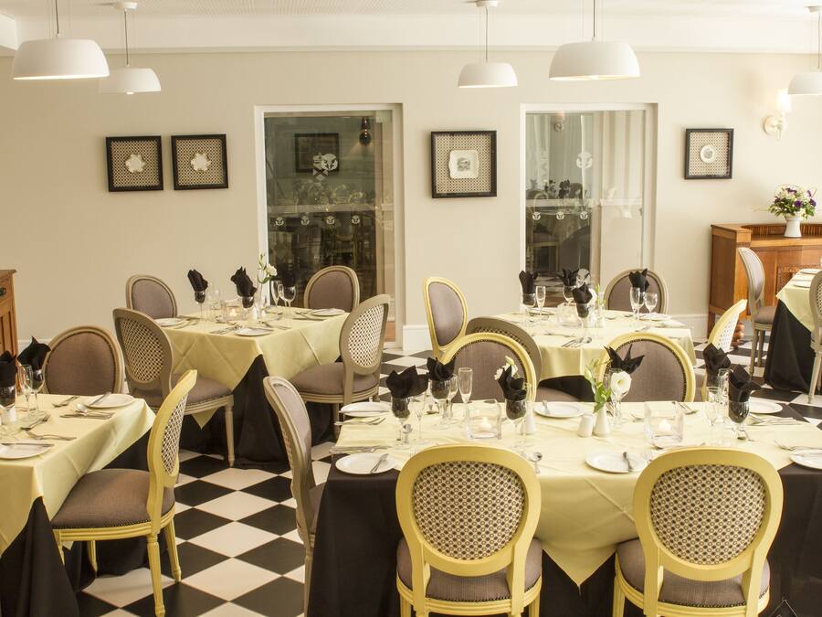 Un comedor con varias mesas dispuestas para una comida, con sillas que tienen asientos y respaldos acolchados, e iluminación colgante.