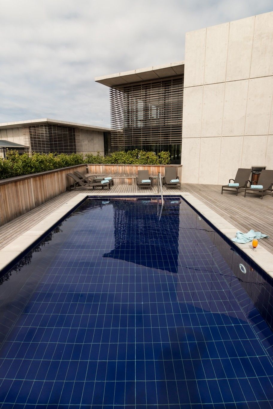 A swimming pool with a tiled deck, lounge chairs, and a modern building with large windows.