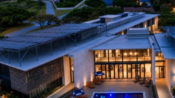 Un edificio moderno con piscina en la azotea, paneles solares y vistas del paisaje circundante.