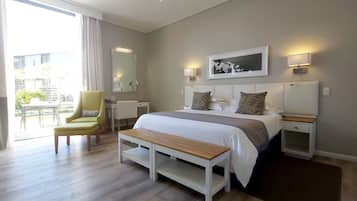 Une chambre d’hôtel avec un lit, des tables de chevet, une chaise, un banc, une grande fenêtre et une vue sur l’extérieur.