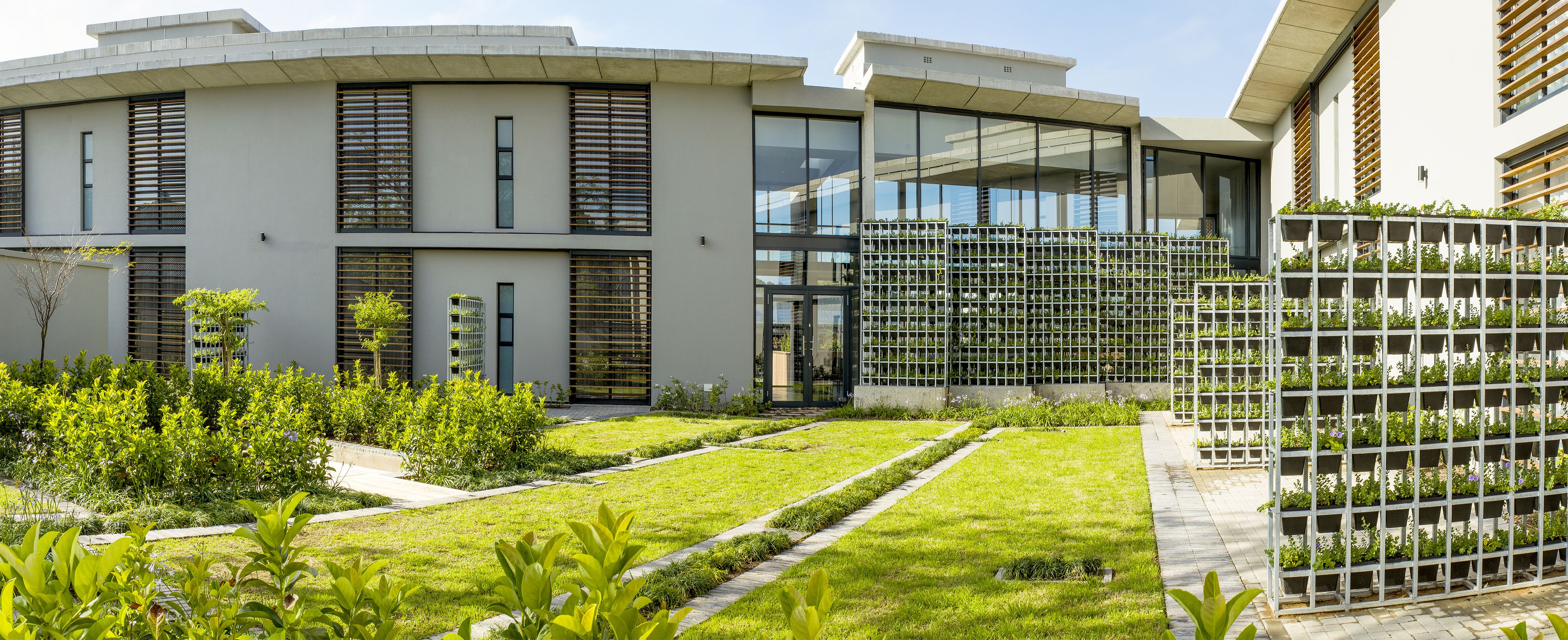 Un edificio moderno con techo plano, amplias ventanas y un jardín cuidado con senderos.