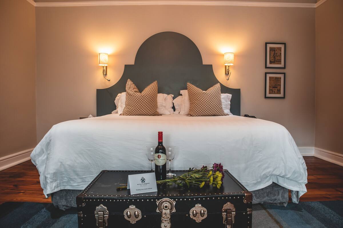 Habitación de hotel con una cama grande, dos lámparas de pared, un cabecero y piso de madera.