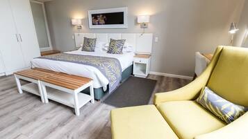 A bedroom with a bed, bedside tables, a bench, a chair, and a wall-mounted TV.