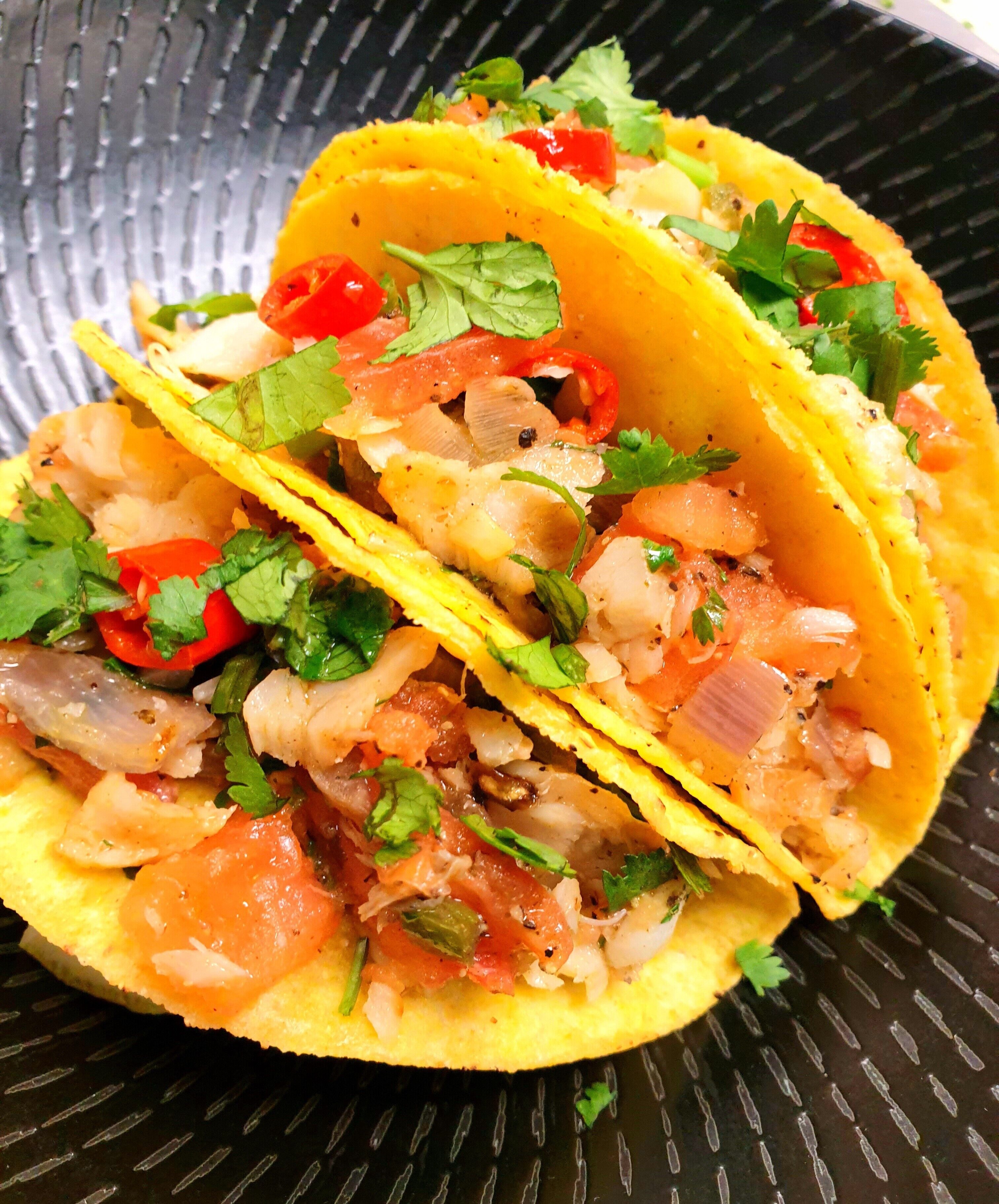 Two tacos with a filling of diced tomatoes, onions, and cilantro, served in yellow corn tortillas on a black plate.