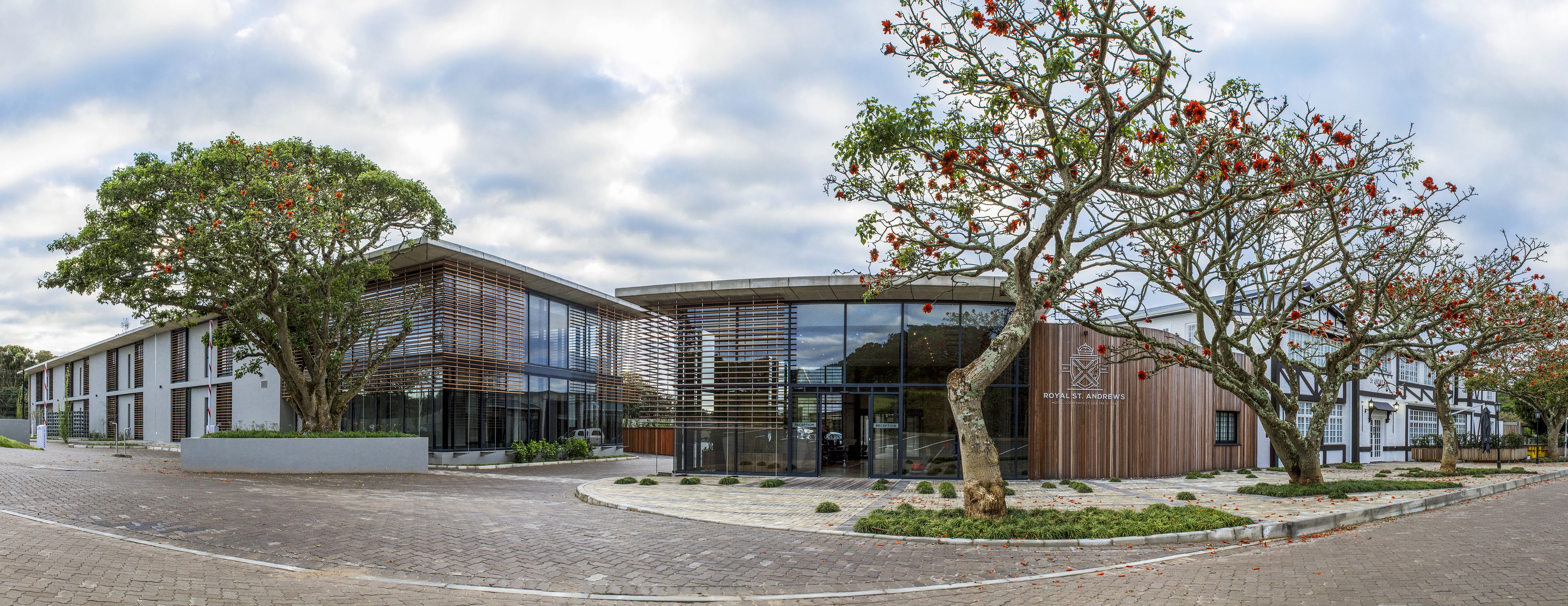 A modern building with a glass facade, a wooden exterior, and a landscaped area with trees and shrubs.