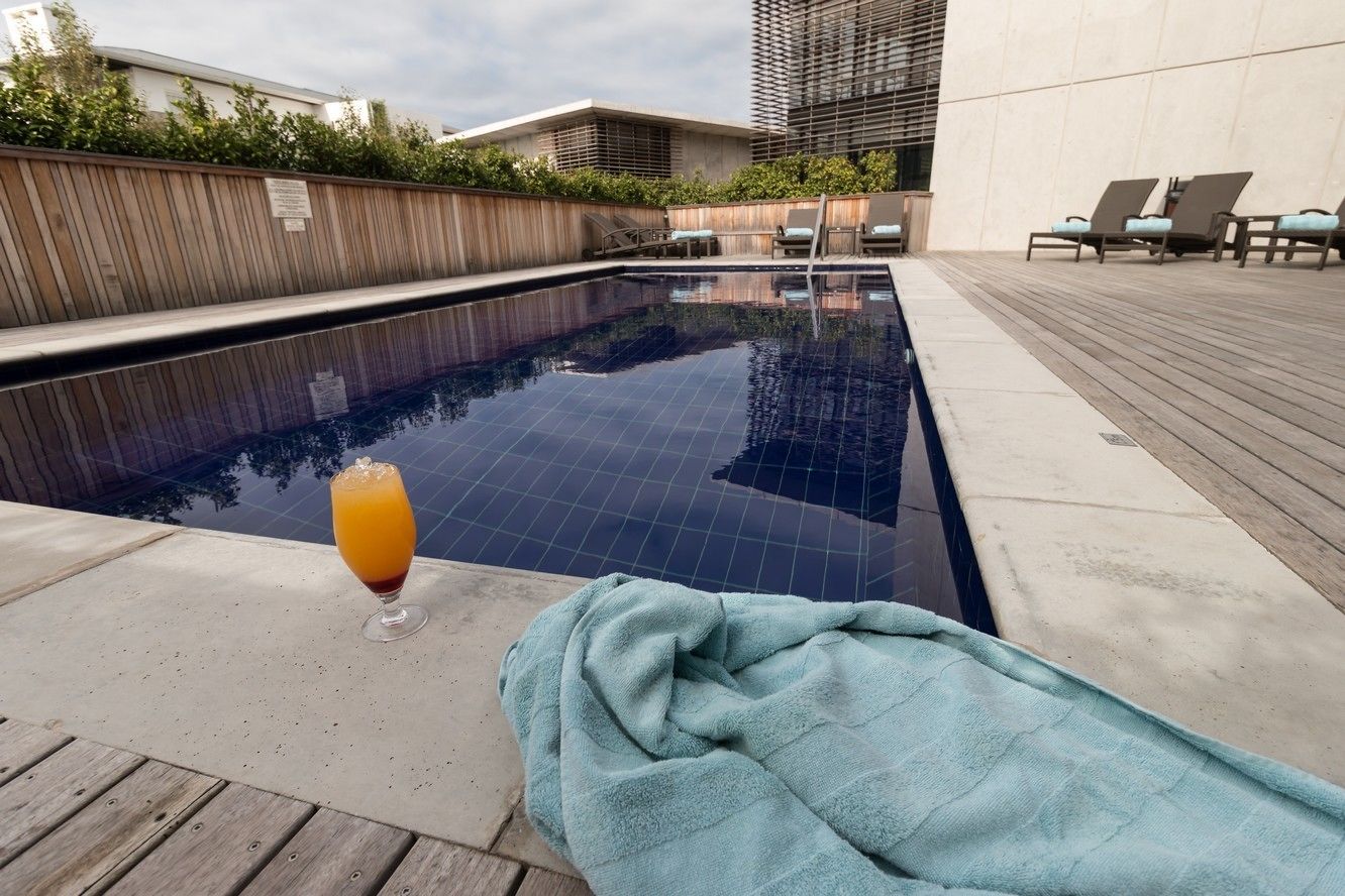 A swimming pool with lounge chairs and a glass of orange juice on the deck.