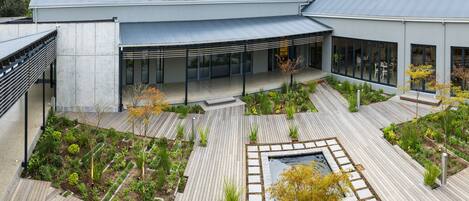 A modern building with a covered outdoor area, a garden with various plants, and a small water feature.