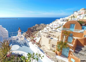 A coastal view with white buildings, a person in a white dress, and a clear blue sea.