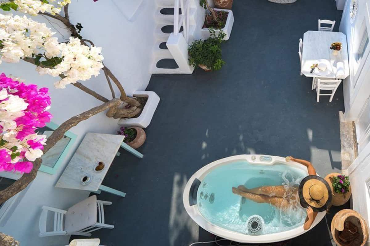 A rooftop pool area with a hot tub, white outdoor furniture, and potted plants.