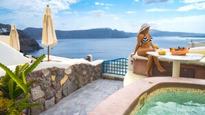 Una mujer con traje de baño sentada a una mesa con una bebida, con vista a una piscina y un paisaje escénico del mar y las montañas.