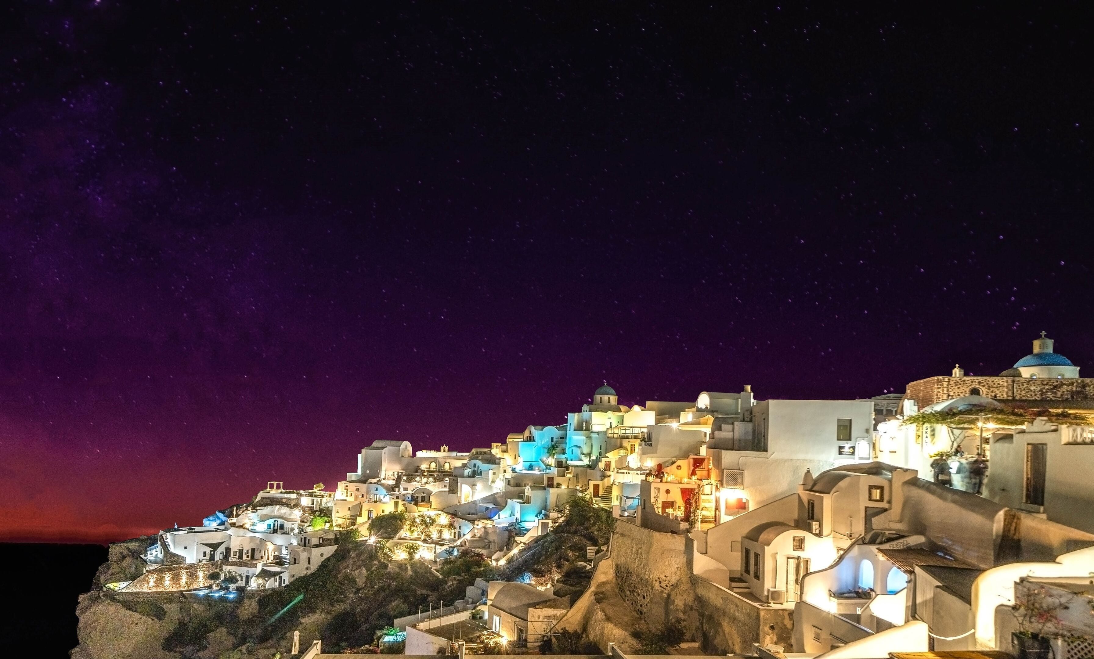 A coastal village with white buildings, steep terrain, and a starry night sky.
