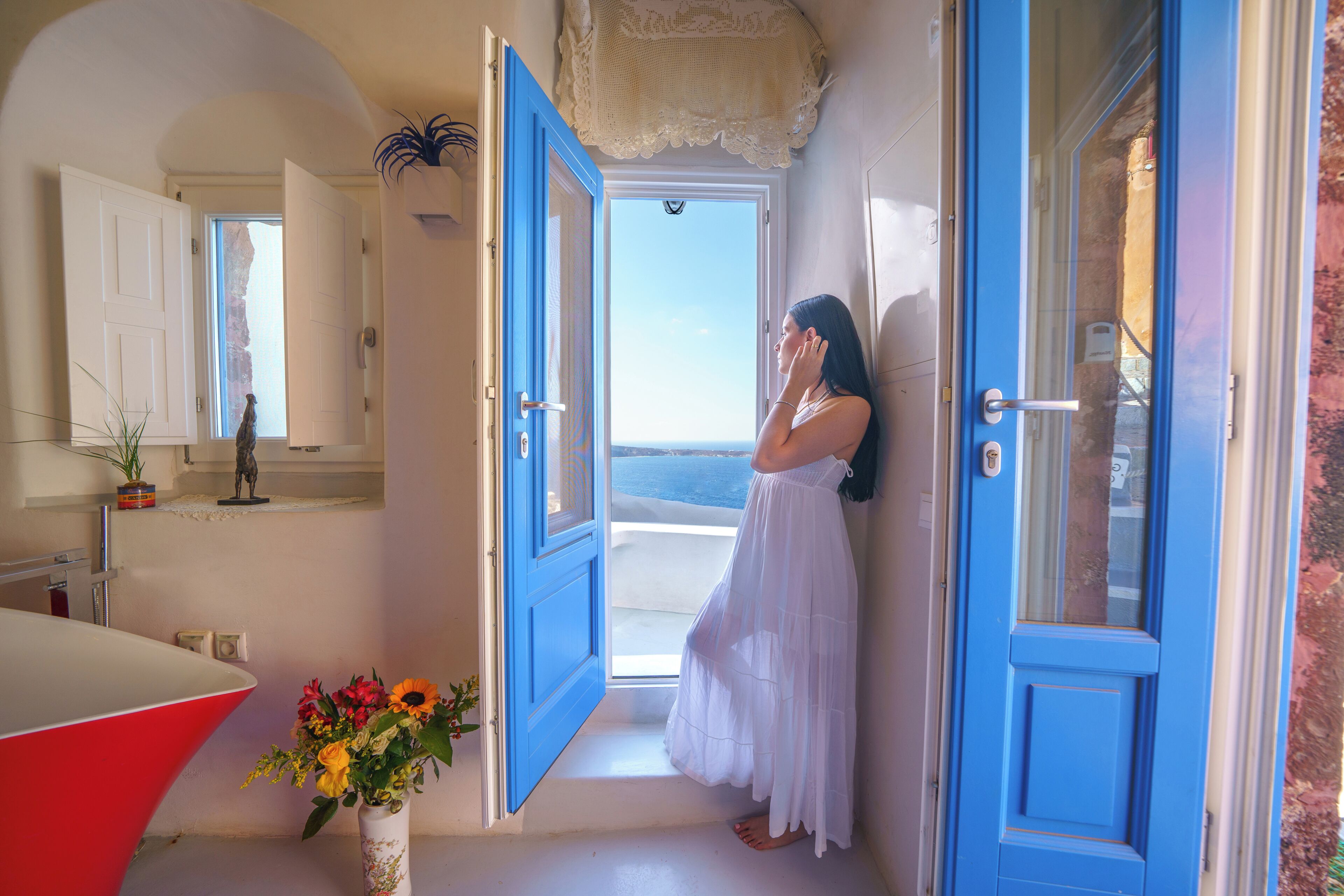 Ein Zimmer mit einem großen Fenster, einer weißen Badewanne und einer Vase mit Blumen.