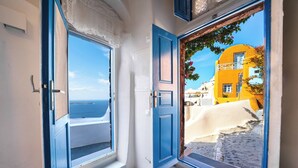Una habitación con dos ventanas abiertas, una con vista al mar y la otra a un edificio amarillo.