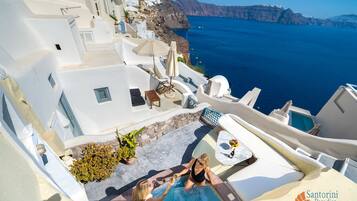 A white-walled building with a pool, outdoor seating, and a view of the sea.