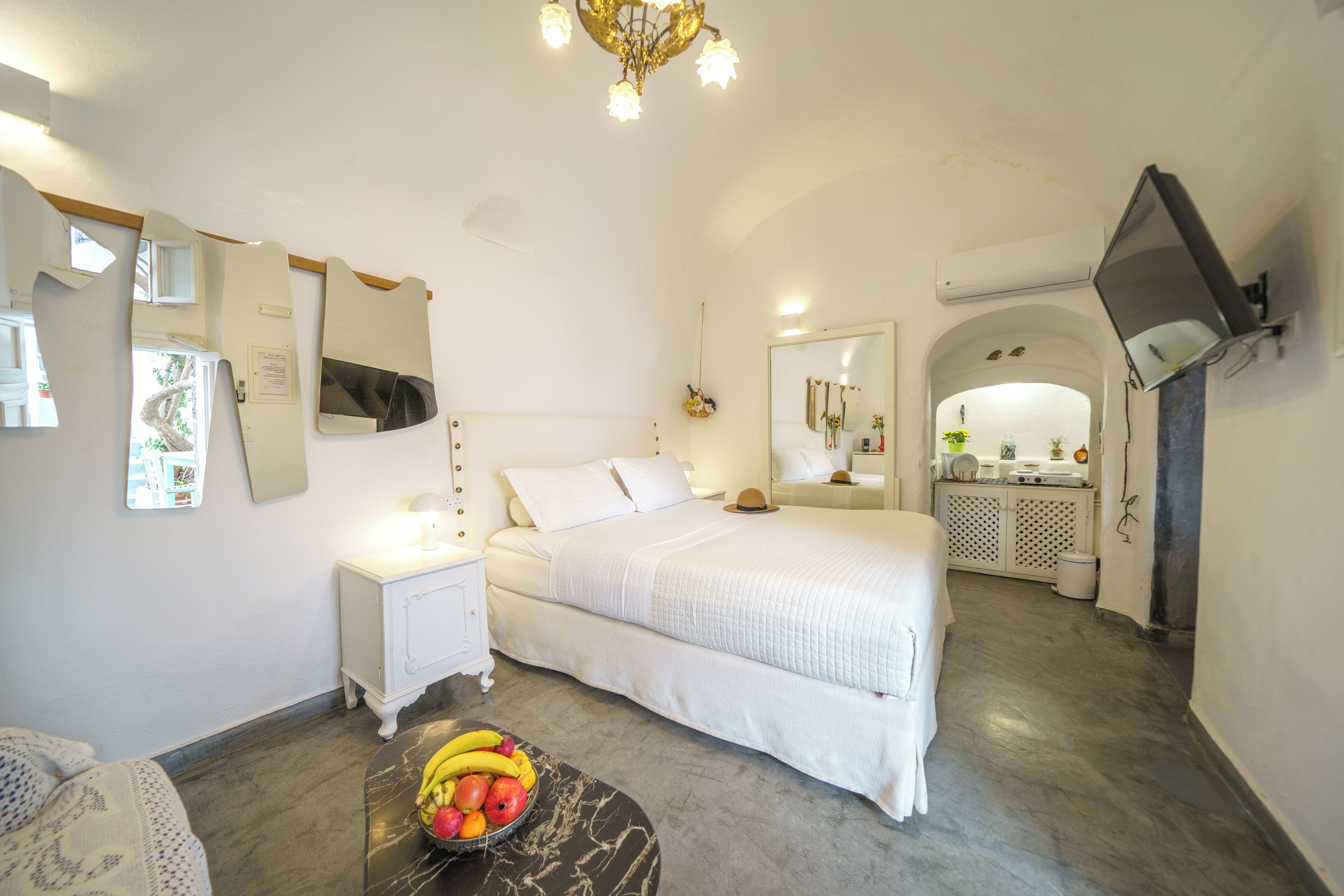 Ein Schlafzimmer mit Bett, Nachttisch, Obstschale und einem an der Wand befestigten Fernseher.