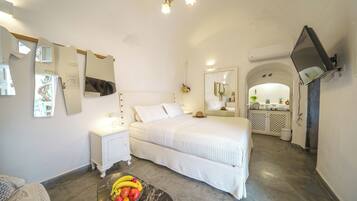 Ein Schlafzimmer mit Bett, Nachttisch, Obstschale und einem an der Wand befestigten Fernseher.