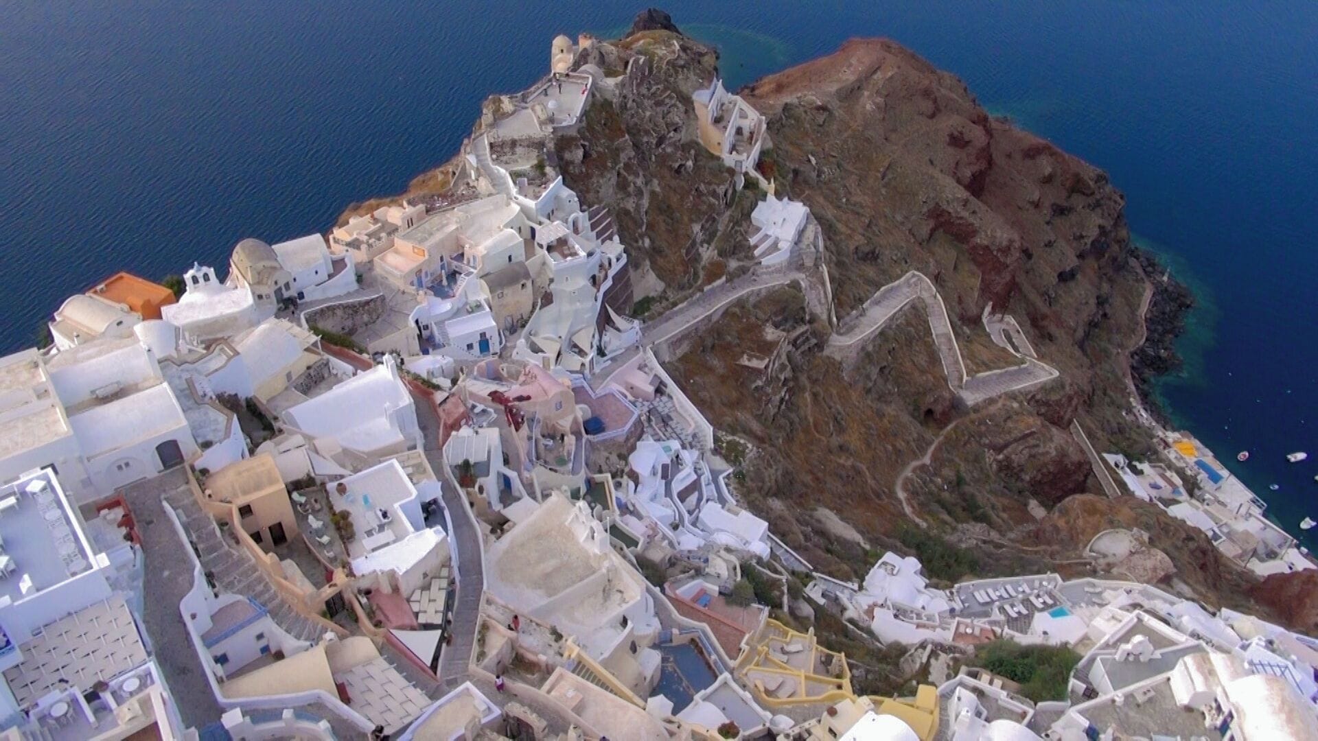 A coastal town with white buildings, narrow streets, and a rocky cliff overlooking the sea.