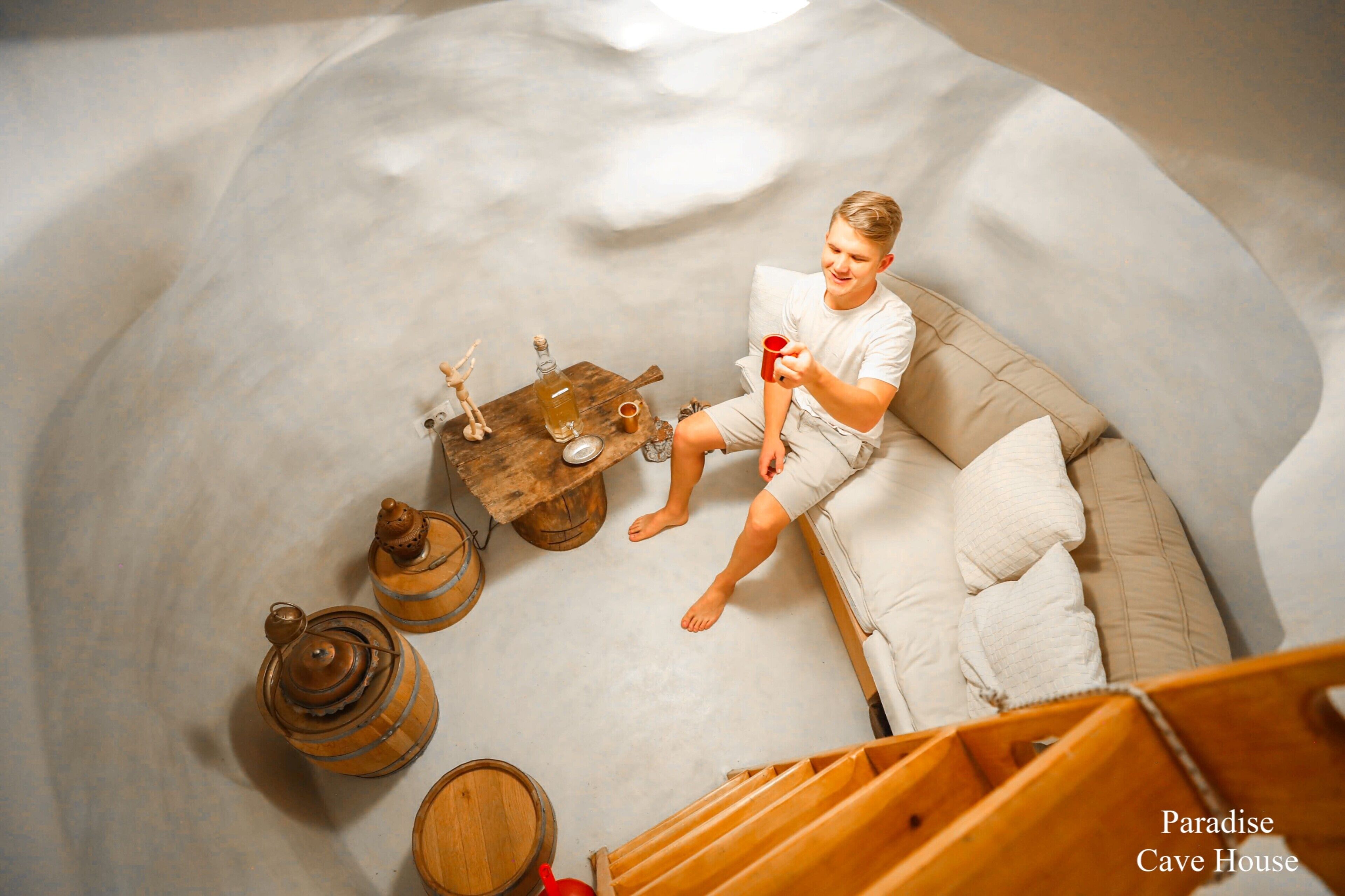 A person sitting on a sofa in a room with wooden barrels and a rustic table.