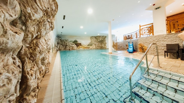 Una piscina interior con paredes de piedra, agua azul cristalina y una escalera que sube a un nivel superior.