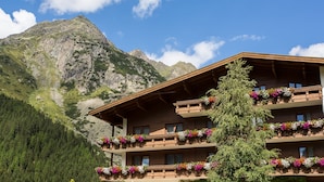 Un edificio de madera de varios pisos con balcones decorados con flores coloridas, con montañas al fondo.