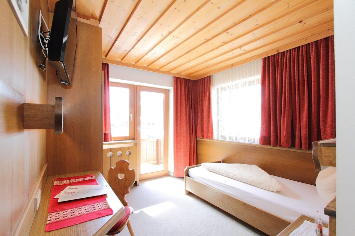 A wooden-paneled room with a bed, a desk, and a window with red curtains.