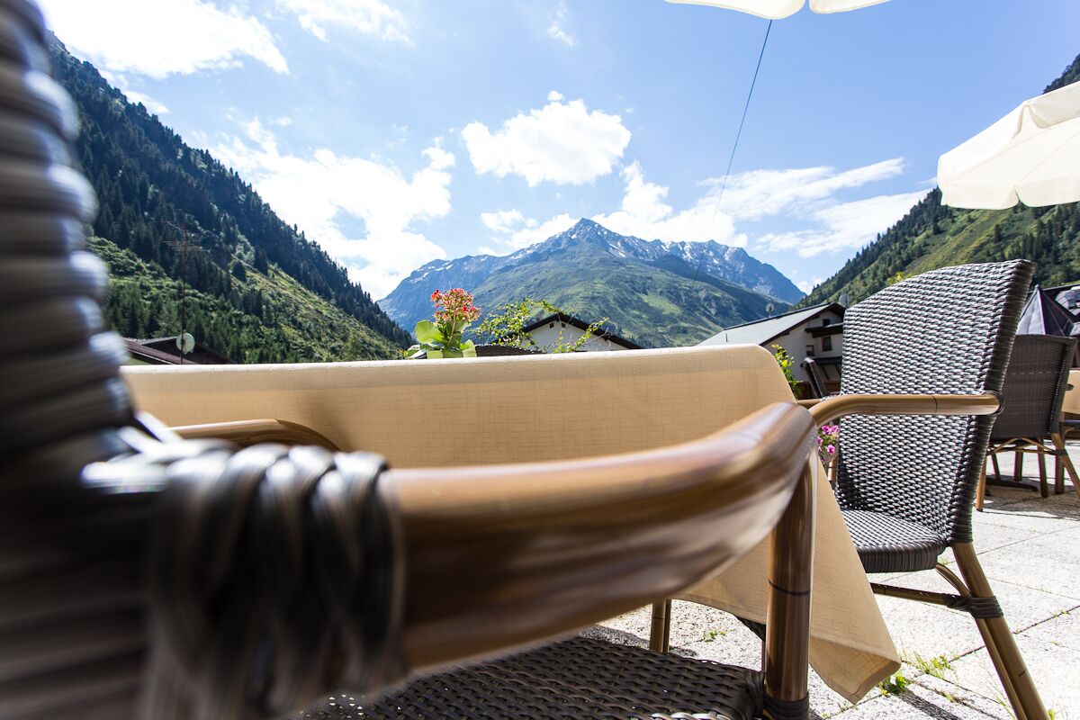 Ein Korbstuhl mit Tisch, einem weißen Sonnenschirm und Blick auf die Berge.