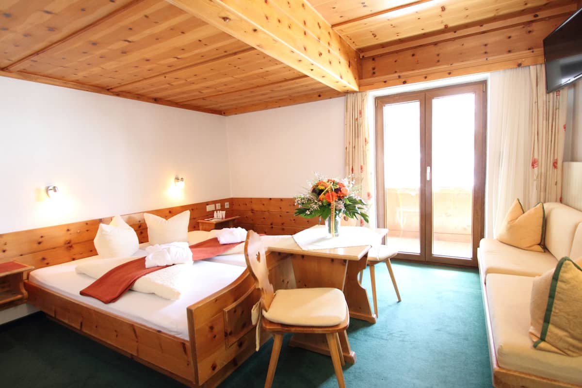 A wooden cabin room with a bed, a desk, a chair, a sofa, and a large window with curtains.