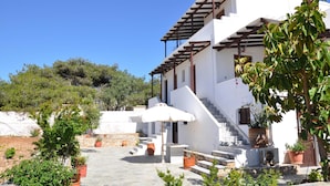 Un edificio blanco con una pérgola de madera, escalones de piedra y plantas en macetas.
