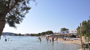 Una playa con gente nadando y tomando el sol, cielo despejado y edificios al fondo.