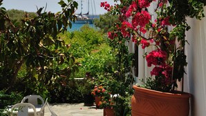 Un patio con plantas en macetas y una silla blanca, una maceta de terracota grande, y vistas de un velero en el agua.