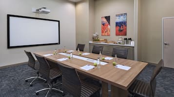 Un salón de conferencias con una larga mesa, sillas, una pantalla de proyector y una estación de café.