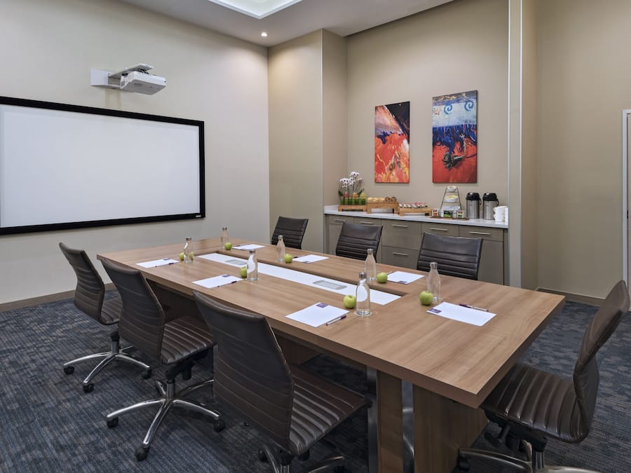 Un salón de conferencias con una larga mesa, sillas, una pantalla de proyector y una estación de café.