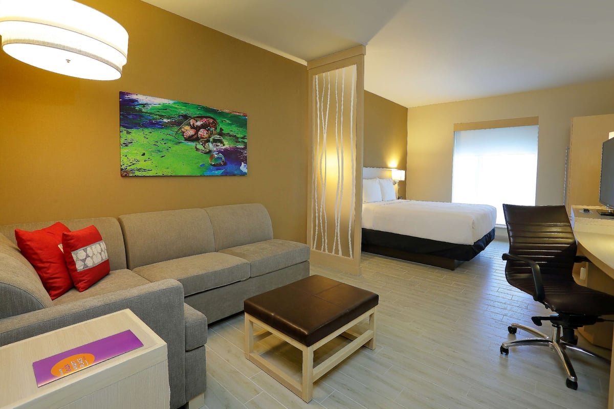 Una habitación de hotel con sofá, cama, escritorio y un cuadro en la pared.