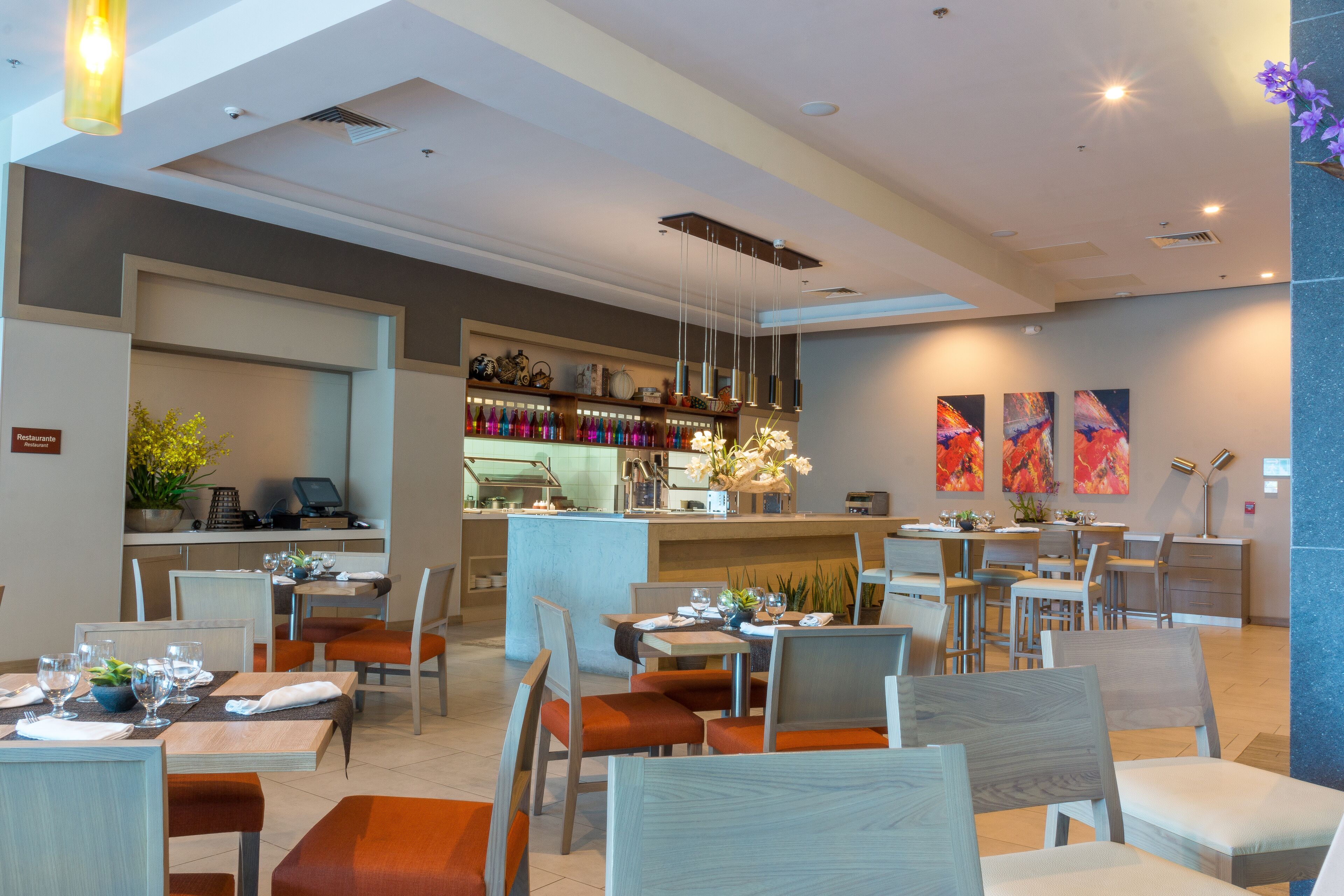 A modern restaurant with multiple dining tables and chairs, a bar area, and artwork on the walls.