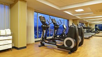 A gym with exercise equipment, a towel rack, and large windows with a city view.