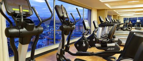A gym with multiple cardio machines, large windows, and a city view.