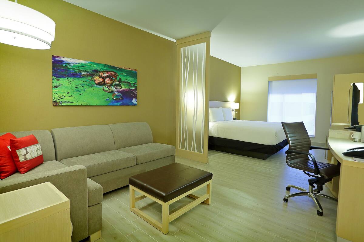 Habitación de hotel con sofá, una mesita, escritorio con silla, cama y un cuadro en la pared.