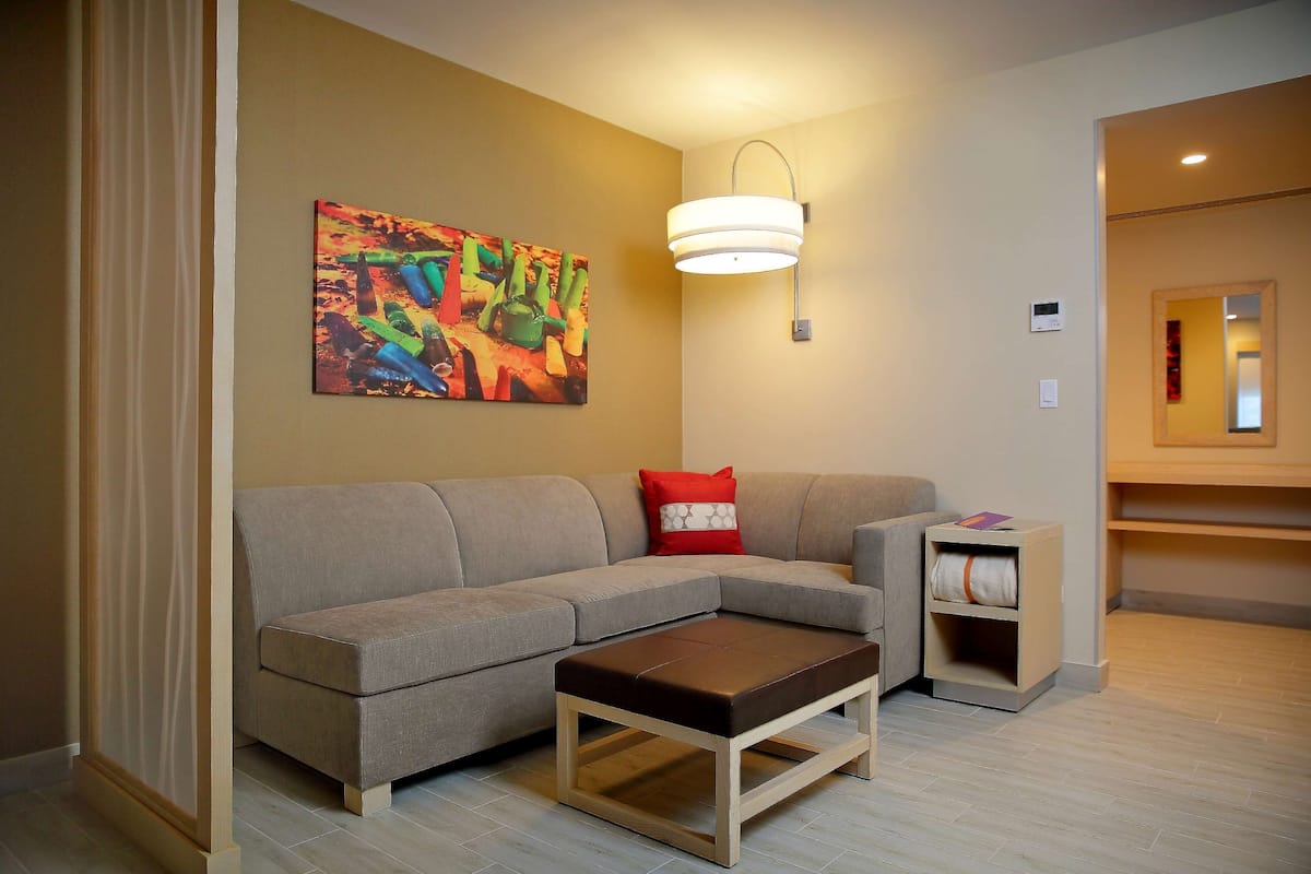 Una sala de estar moderna con un sofá modular, una mesa de centro de madera, una lámpara de pared y un cuadro abstracto colorido.