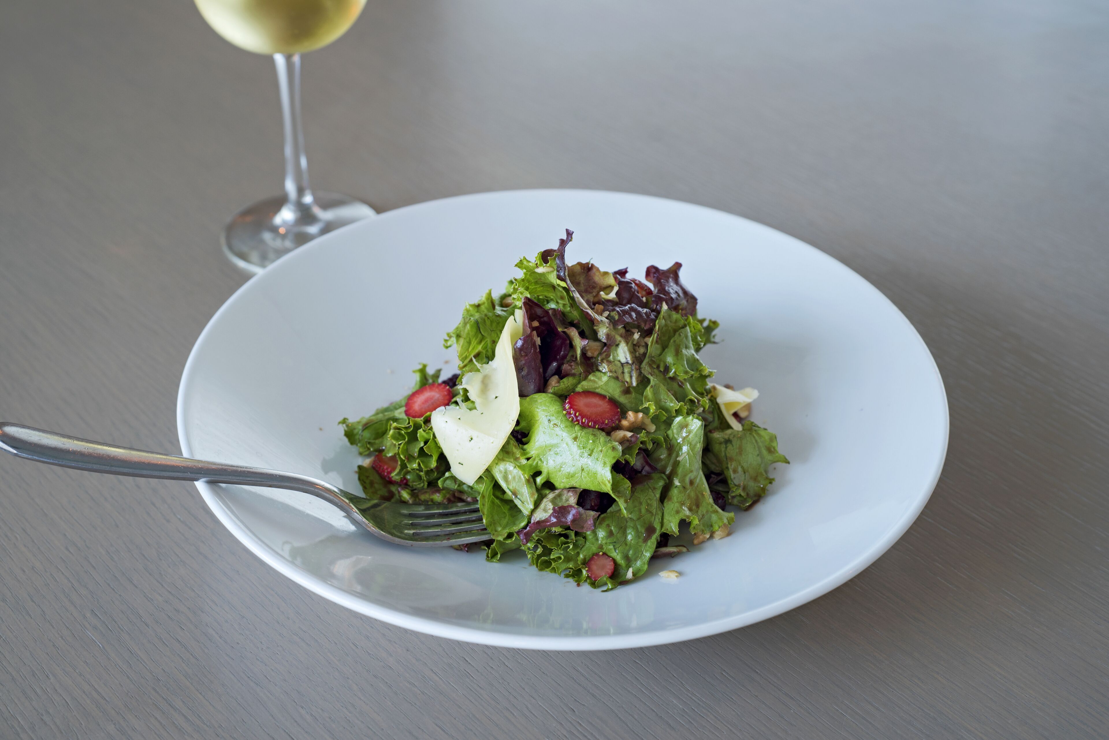 A white plate with a salad and a fork on a table.