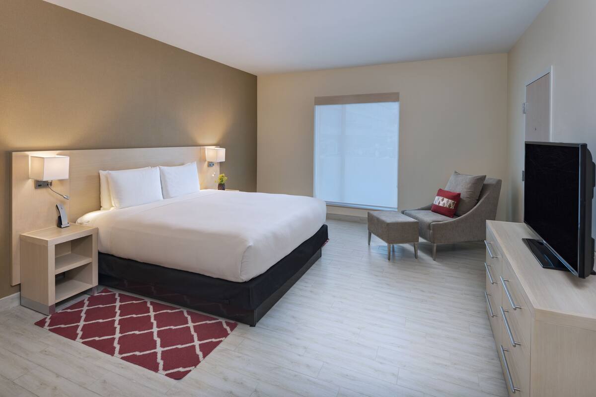 Una habitación de hotel moderna con una cama grande, televisor, una silla y un escritorio.