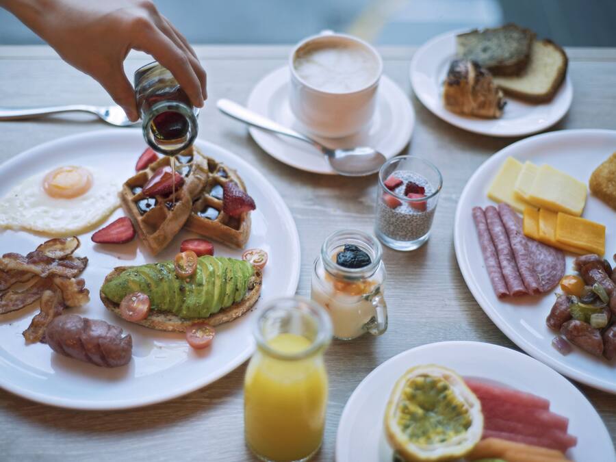 Une table de petit-déjeuner avec divers plats, notamment des gaufres, des œufs, du bacon et des toasts.