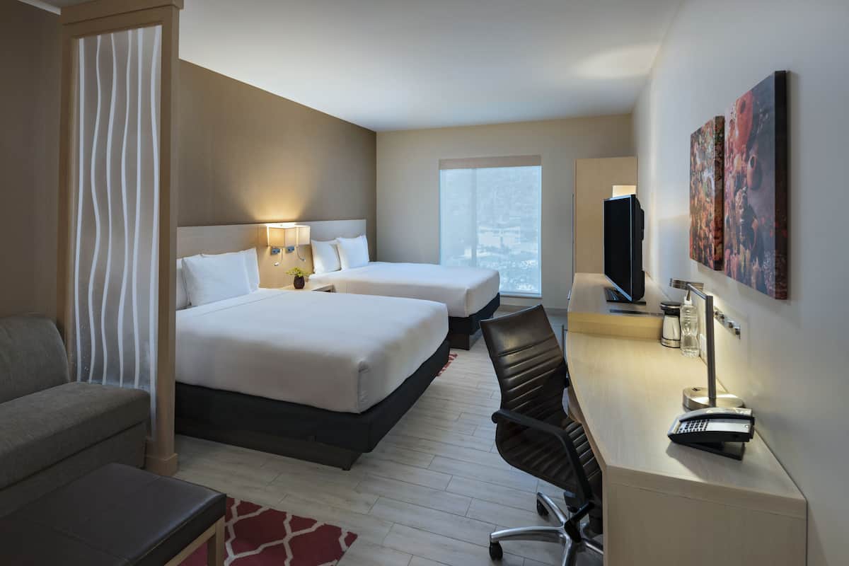 Habitación de hotel con dos camas, un escritorio con silla, televisión y obras de arte en la pared.