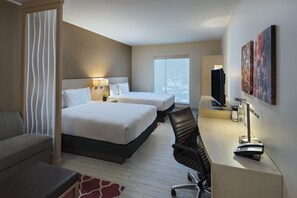 Habitación de hotel con dos camas, un escritorio con silla, televisión y obras de arte en la pared.