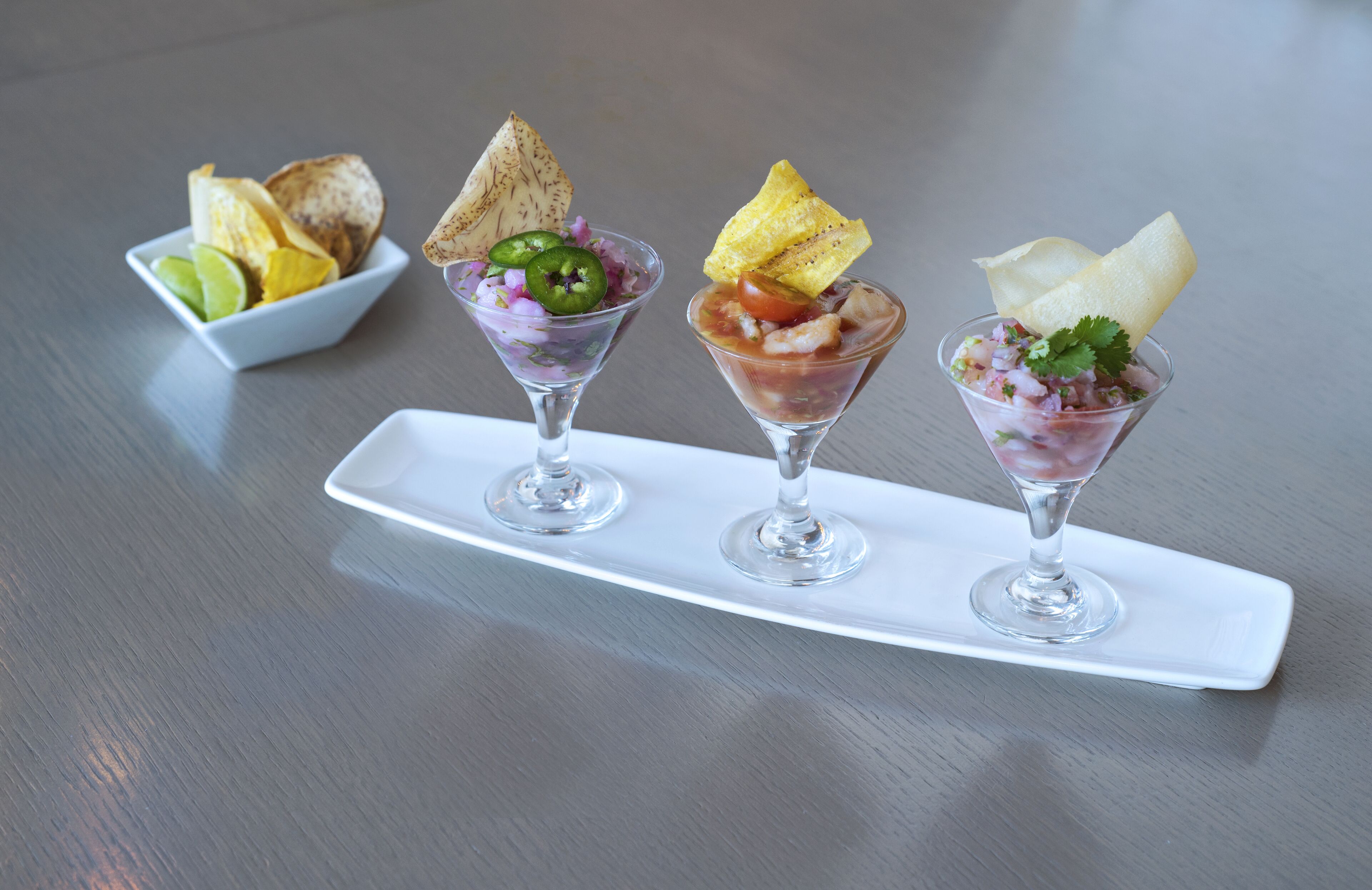 Three martini glasses with different garnishes on a white rectangular plate.