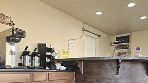A coffee shop interior with a wooden counter, a coffee machine, and a sign indicating a check-out time. - Redrock Country Inn (Kanab)