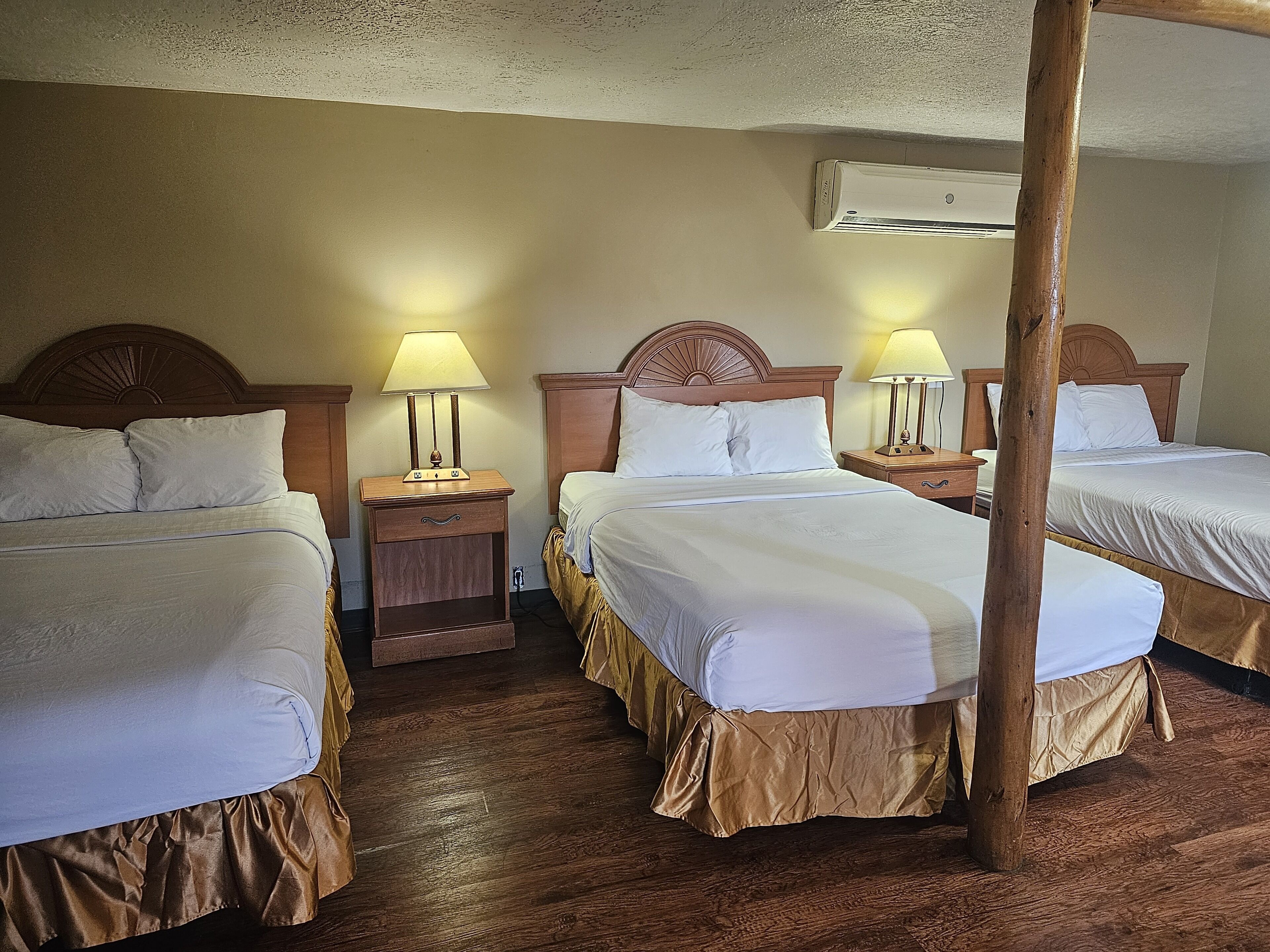 Ein Hotelzimmer mit zwei Betten, Holz-Kopfteilen, Nachttischen mit Lampen und einer Klimaanlage an der Wand.