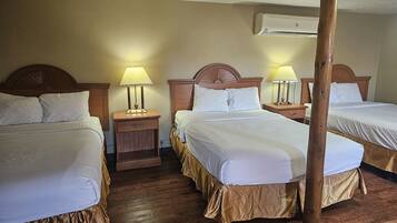 Habitación de hotel con dos camas, cabeceros de madera, mesitas de noche con lámparas y un equipo de aire acondicionado en la pared.